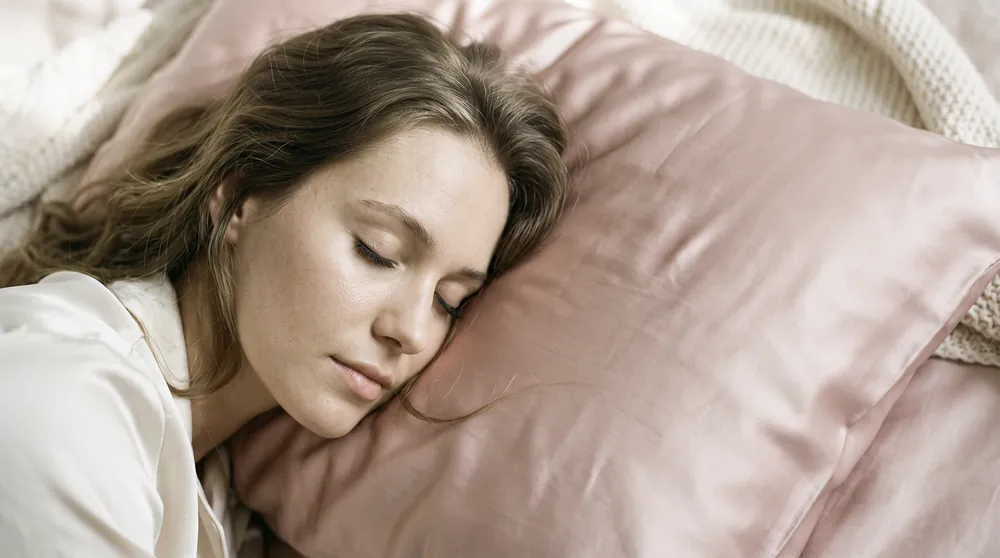 A woman asleep on a blush silk pillowcase